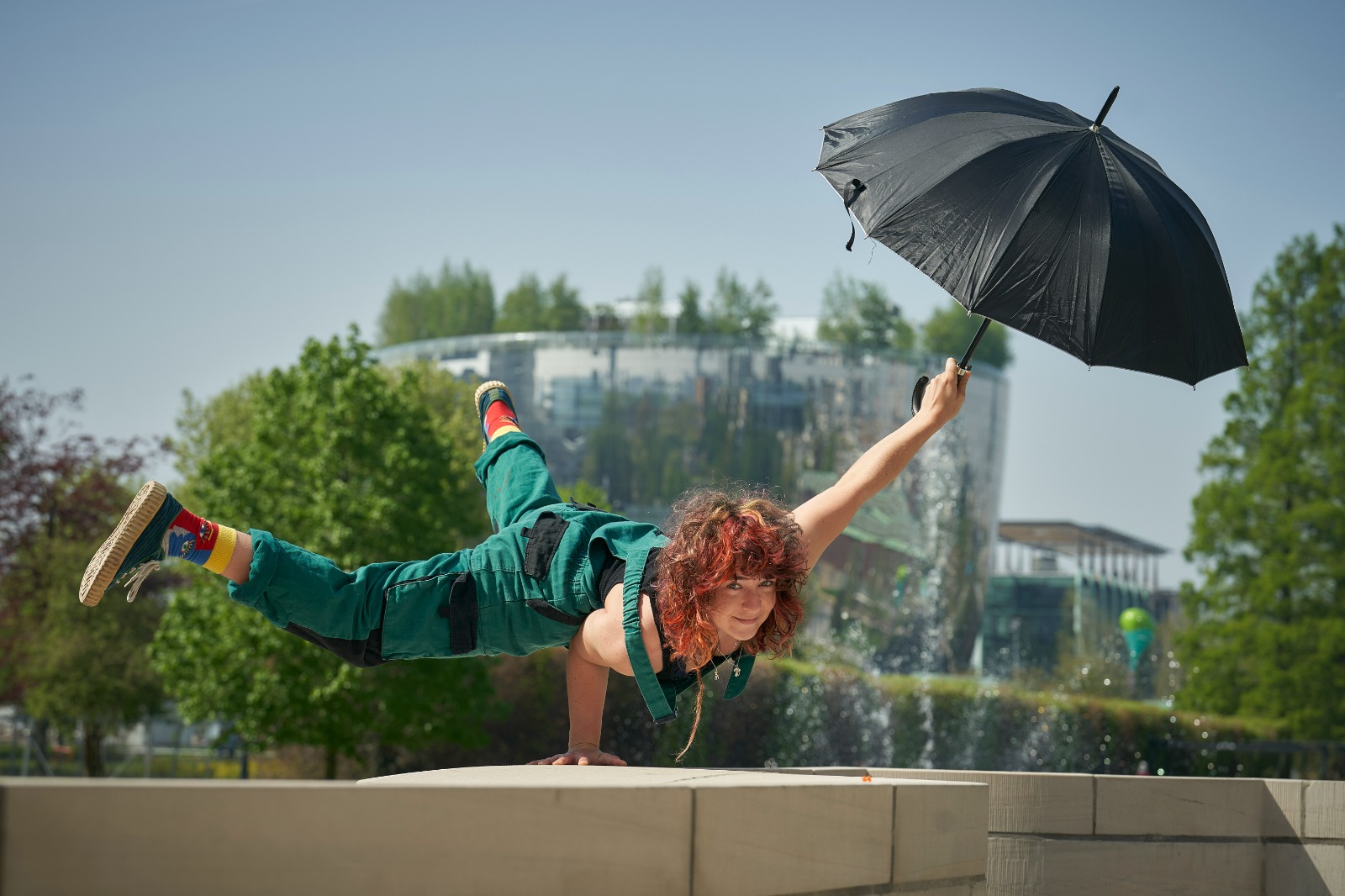Hannah performing a one-handed handstand with an umbrella in the other hand.